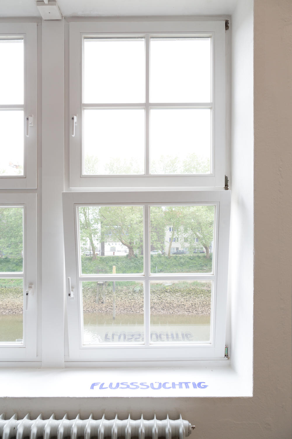 Ein Fenster mit Blick auf die Weser, wo auf der Fensterbank "Flusssüchtig" steht